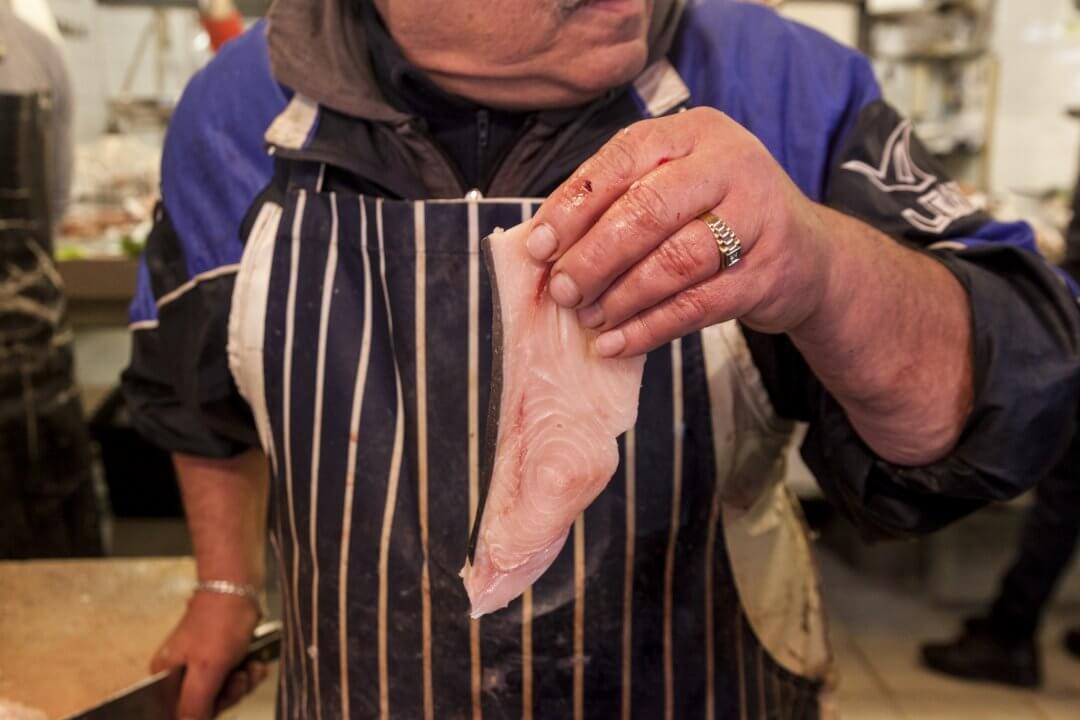 a fisherman has in his hand a slice of fish and in the other hand a big knife
